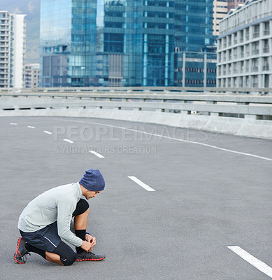 Buy stock photo Shot of a young man tying up his shoelaces before a run through the city