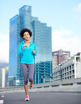 Buy stock photo Shot of a young woman jogging alone through empty city streets