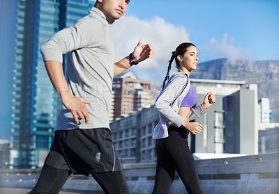 Buy stock photo Shot of two friends jogging together through the city streets