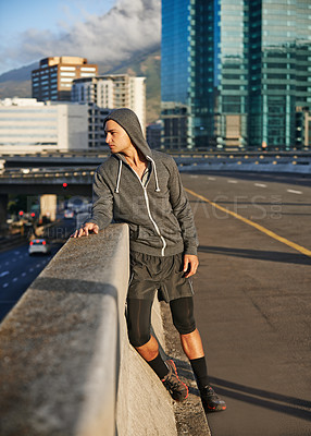Buy stock photo Shot of a young male jogger taking a breather while out for a run in the early morning