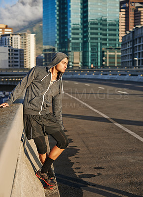 Buy stock photo Shot of a young male jogger taking a breather while out for a run in the early morning