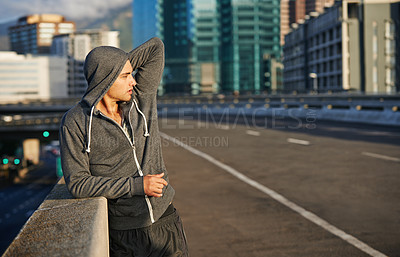 Buy stock photo Shot of a young male jogger taking in the sunrise while out for a run through the city