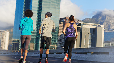 Buy stock photo Rearview shot of three young joggers out for a run in the city streets