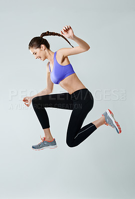 Buy stock photo Side view shot of a sporty young woman jumping against a gray background