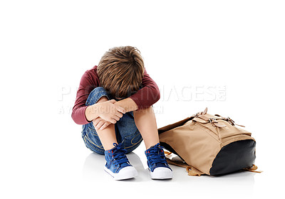 Buy stock photo Studio shot of a little boy with his head buried in his knees sitting next to his schoolbag against a white background