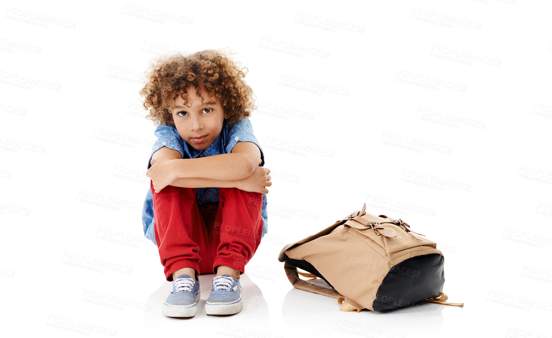 Buy stock photo Studio shot of a cute little boy hugging his knees next to his schoolbag against a white background
