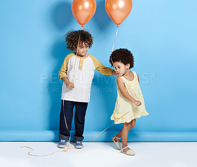 Buy stock photo Shot of a little girl and boy holding a balloon over a blue background