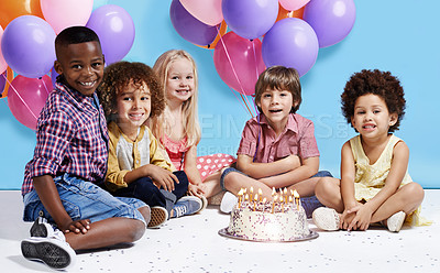 Buy stock photo Shot of a group of children sitting around a birthday cake with bunch of balloons in the background