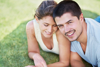 Buy stock photo An attractive young couple lying on the grass together and smiling
