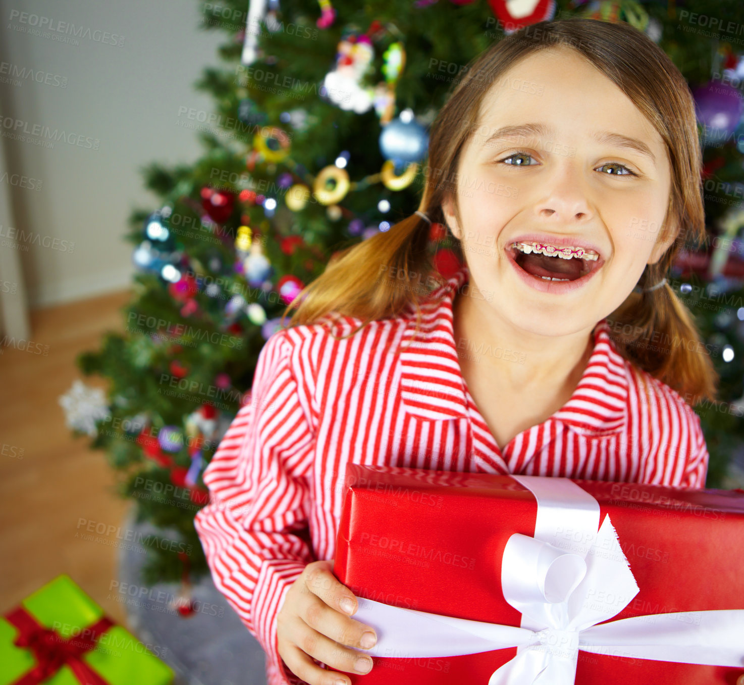 Buy stock photo Portrait of an excited girl with braces on waiting to unwrap her present by the christmas tree