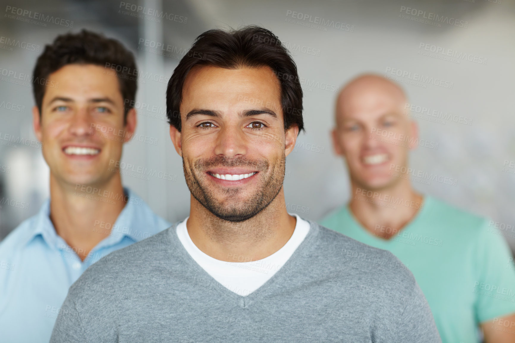 Buy stock photo Shot of a young man standing in an office with male colleagues in the background