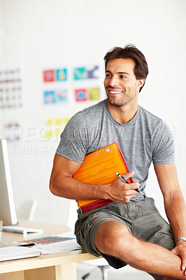 Buy stock photo A smiling handsome man sitting on an office desk with folder under his arm and pen in hand