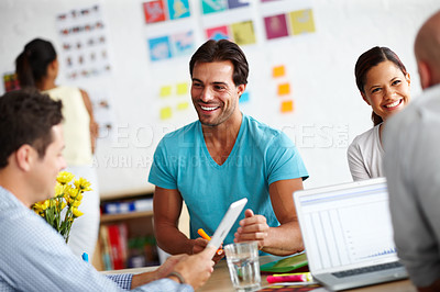 Buy stock photo A handsome young man sitting at a table in a working a environment and sharing ideas with his colleagues