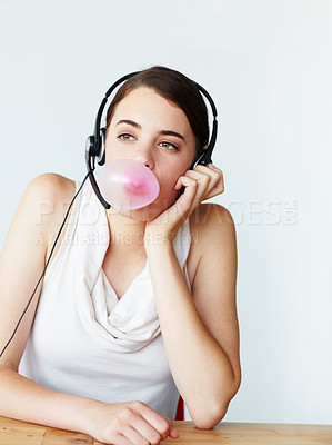 Buy stock photo A beautiful young customer service representative sitting at a table and blowing a bubble while chewing bubblegum