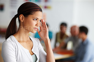 Buy stock photo Shot of a young female professional with her hand to her temple looking in pain with coworkers in the background