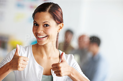 Buy stock photo Portrait of an attractive young professional smiling and giving two thumbs-up while colleagues work in the background