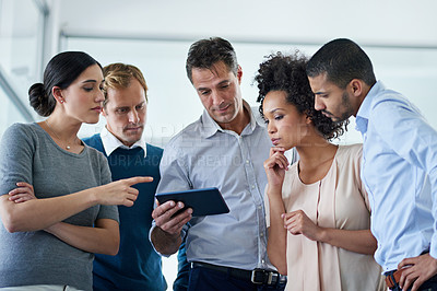 Buy stock photo Shot of a group of colleagues looking at a digital tablet together