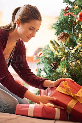 Buy stock photo Shot of an attractive young woman looking through presents under a christmas tree