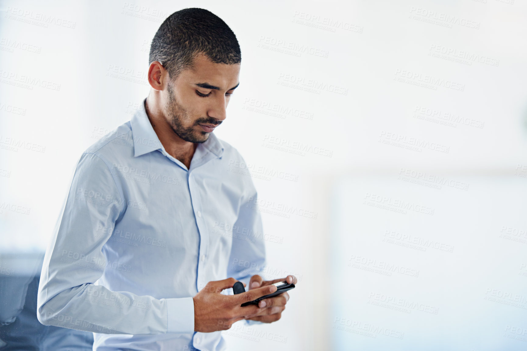 Buy stock photo Shot of a young businessman sending a text message while standing in an office