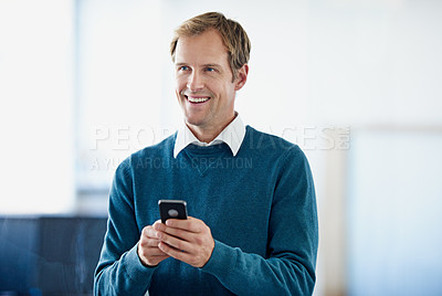 Buy stock photo Shot of a young businessman sending a text message while standing in an office