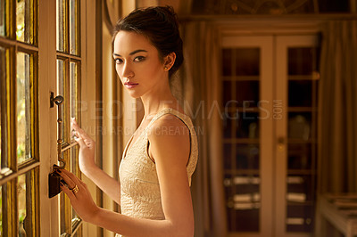 Buy stock photo Portrait of a beautiful and elegant young woman standing by a window