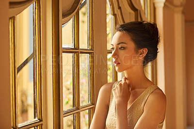 Buy stock photo Shot of a beautiful and elegant young woman standing by a window