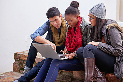 Buy stock photo Shot of a group of university students using a laptop while sitting on campus