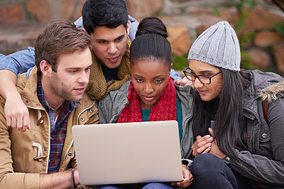 Buy stock photo Shot of a group of college students using a laptop while sitting on campus