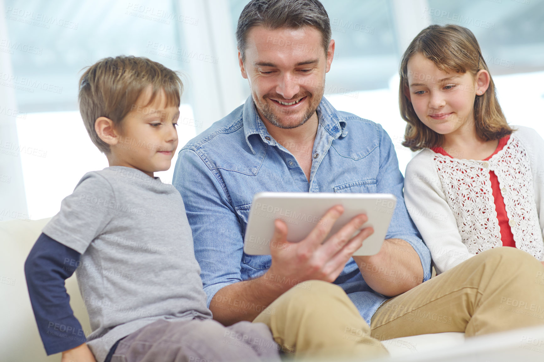 Buy stock photo Shot of a loving father using a digital tablet with his son and daughter at home