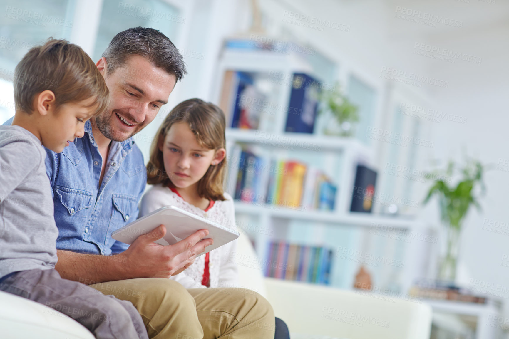 Buy stock photo Shot of a loving father using a digital tablet with his son and daughter at home