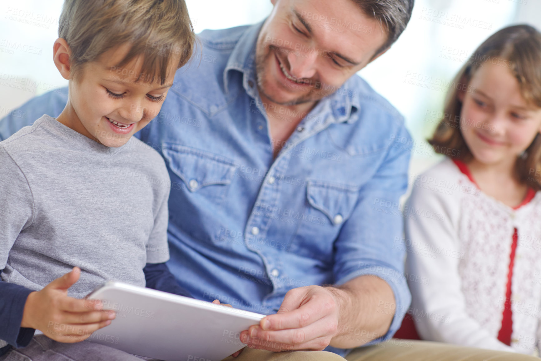 Buy stock photo Shot of a loving father using a digital tablet with his son and daughter at home