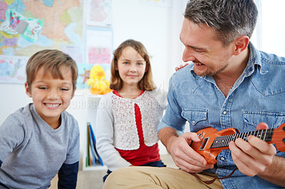 Buy stock photo Shot of a happy father playing the guitar for his son and daughter at home