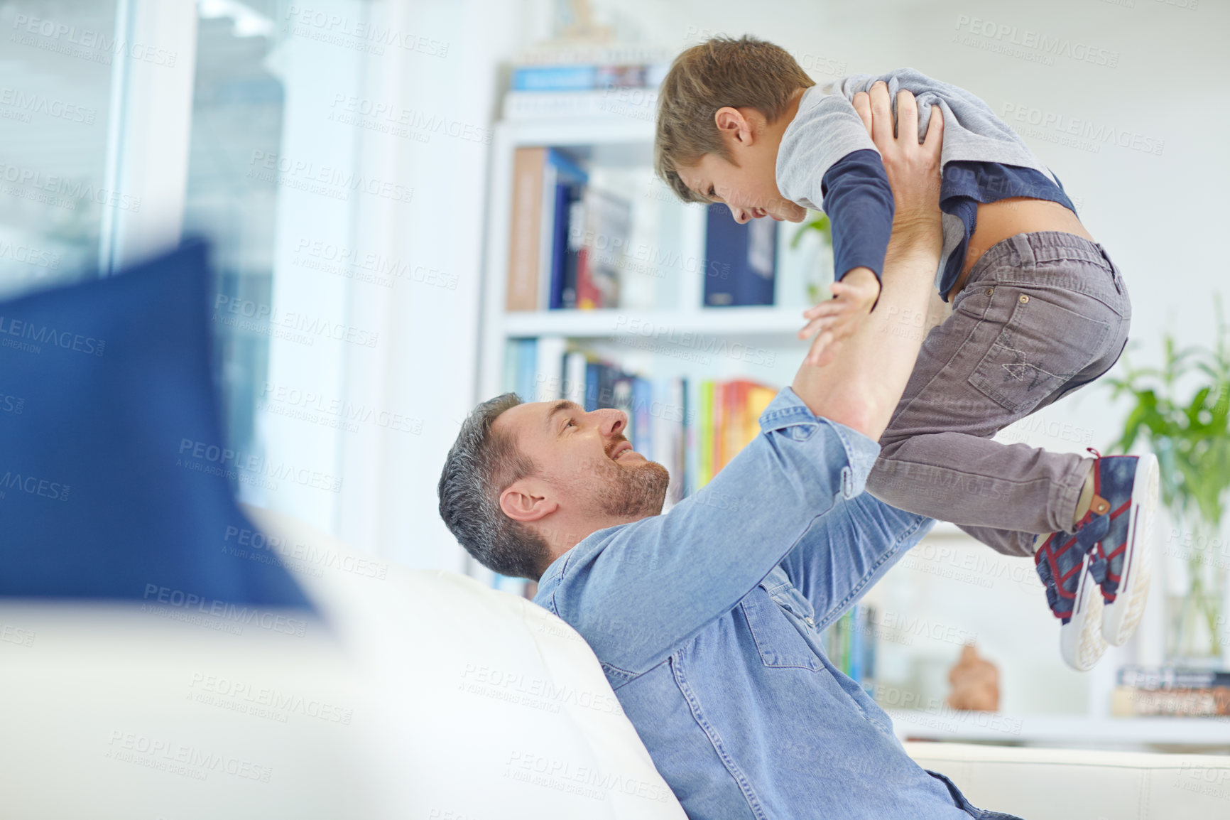 Buy stock photo Shot of a loving father sitting on the sofa while playfully lifting his son into the air