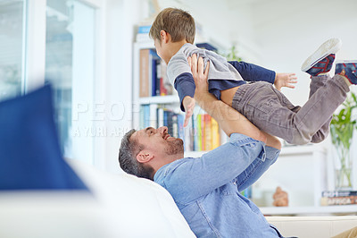 Buy stock photo Shot of a loving father sitting on the sofa while playfully lifting his son into the air