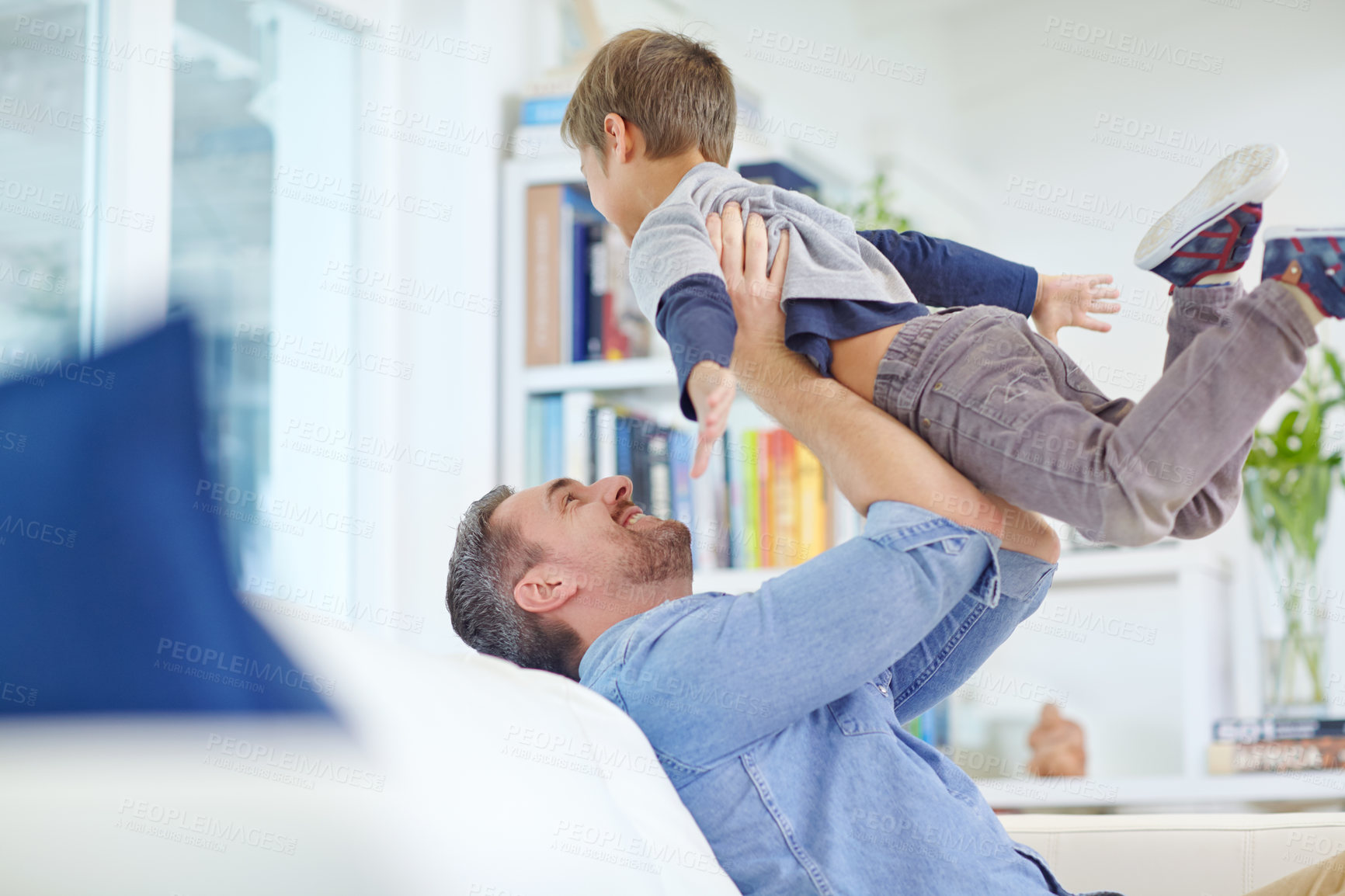 Buy stock photo Shot of a loving father sitting on the sofa while playfully lifting his son into the air