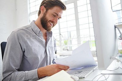 Buy stock photo Shot of a young designer holding paperwork while sitting in front of his computer