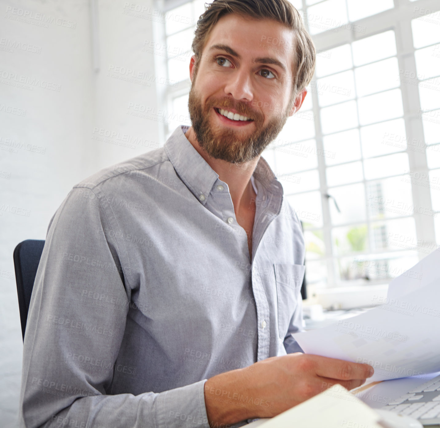 Buy stock photo Shot of a young designer holding paperwork while sitting in front of his computer