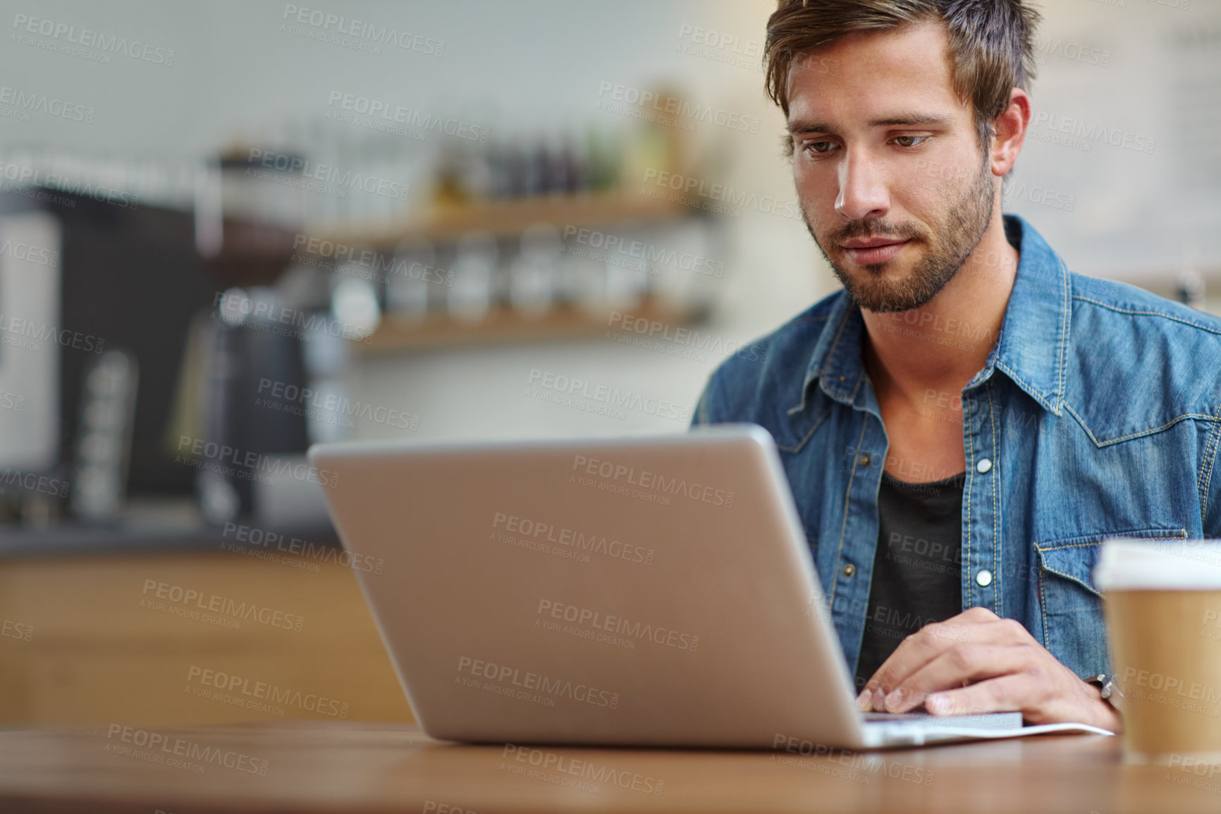 Buy stock photo Shot of a handsome young man working on his laptop in a coffee shop