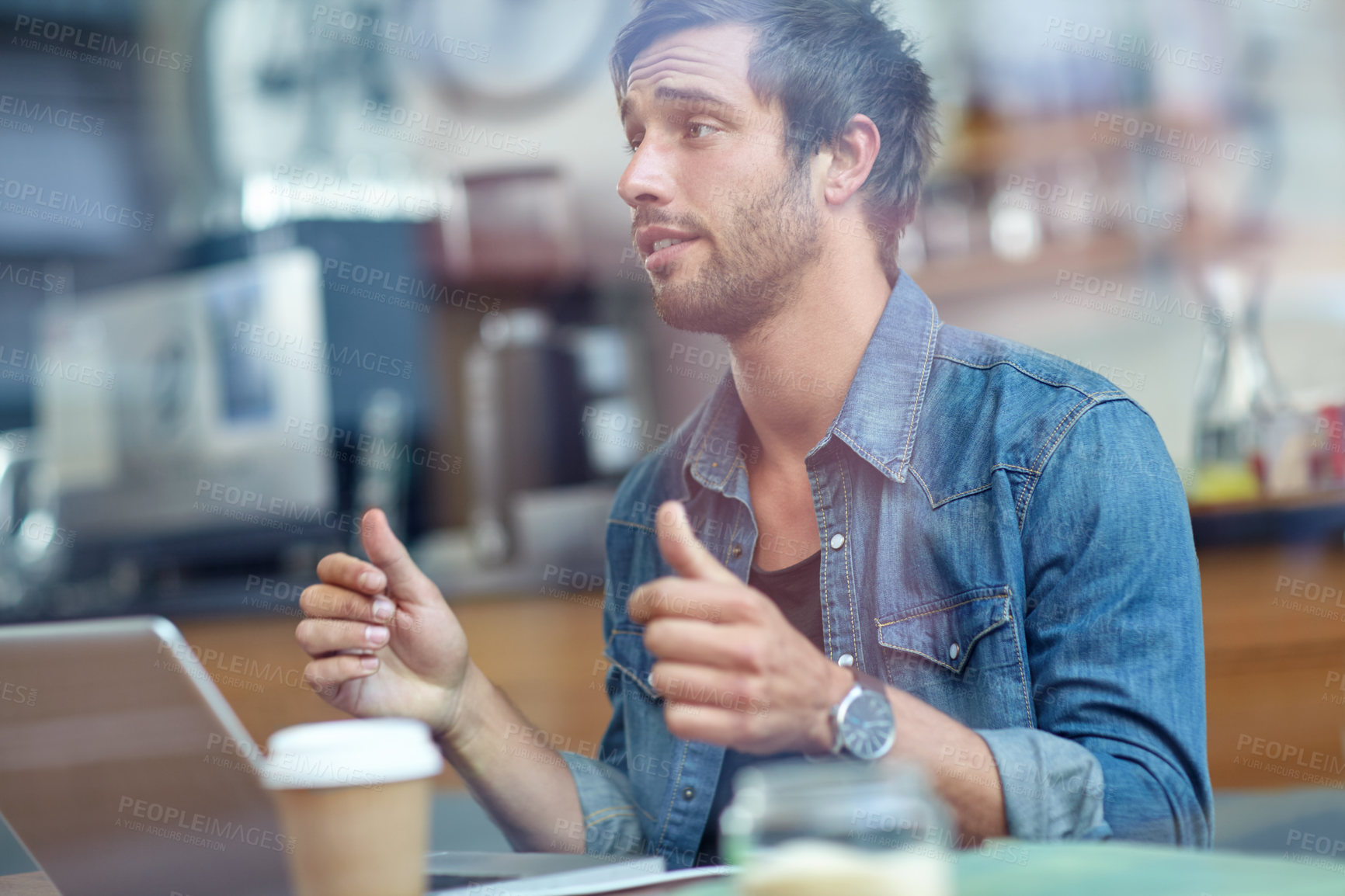 Buy stock photo Shot of a young man sitting in a coffee shop showing thumbs up to someone off-camera 