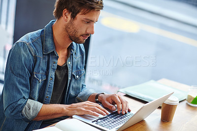 Buy stock photo Shot of a handsome young man working on his laptop in a coffee shop