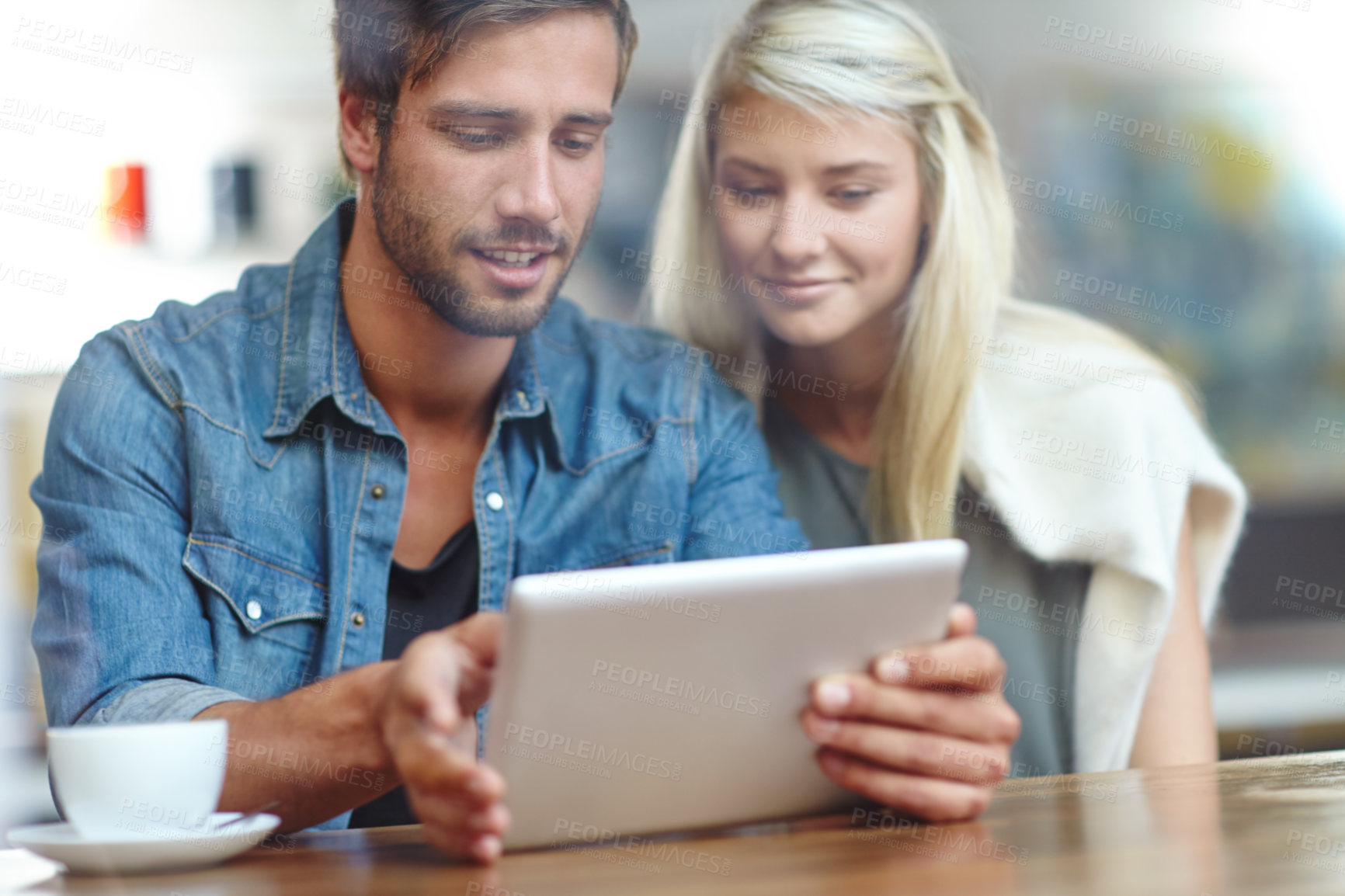 Buy stock photo Shot of a young couple looking at someting on a tablet while on a coffee date