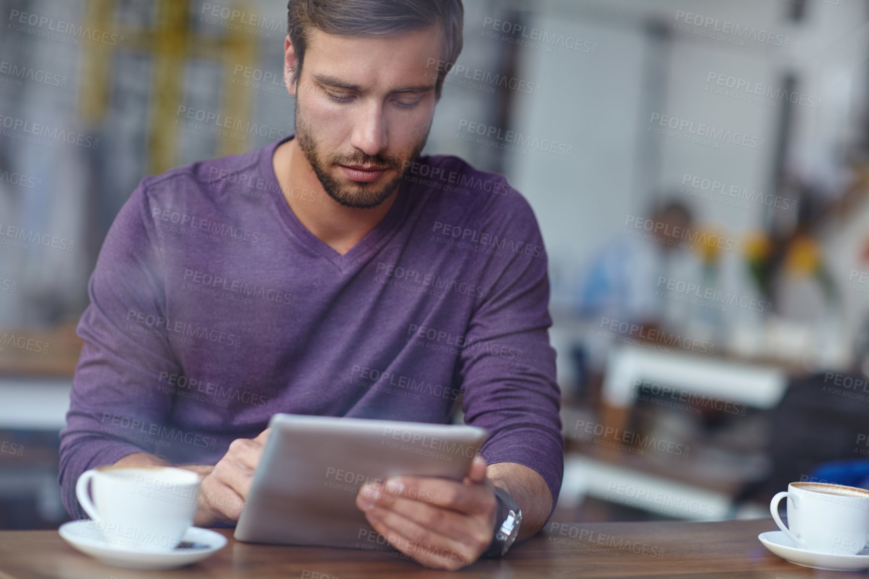 Buy stock photo Shot of a handsome young man using his tablet at a coffee shop