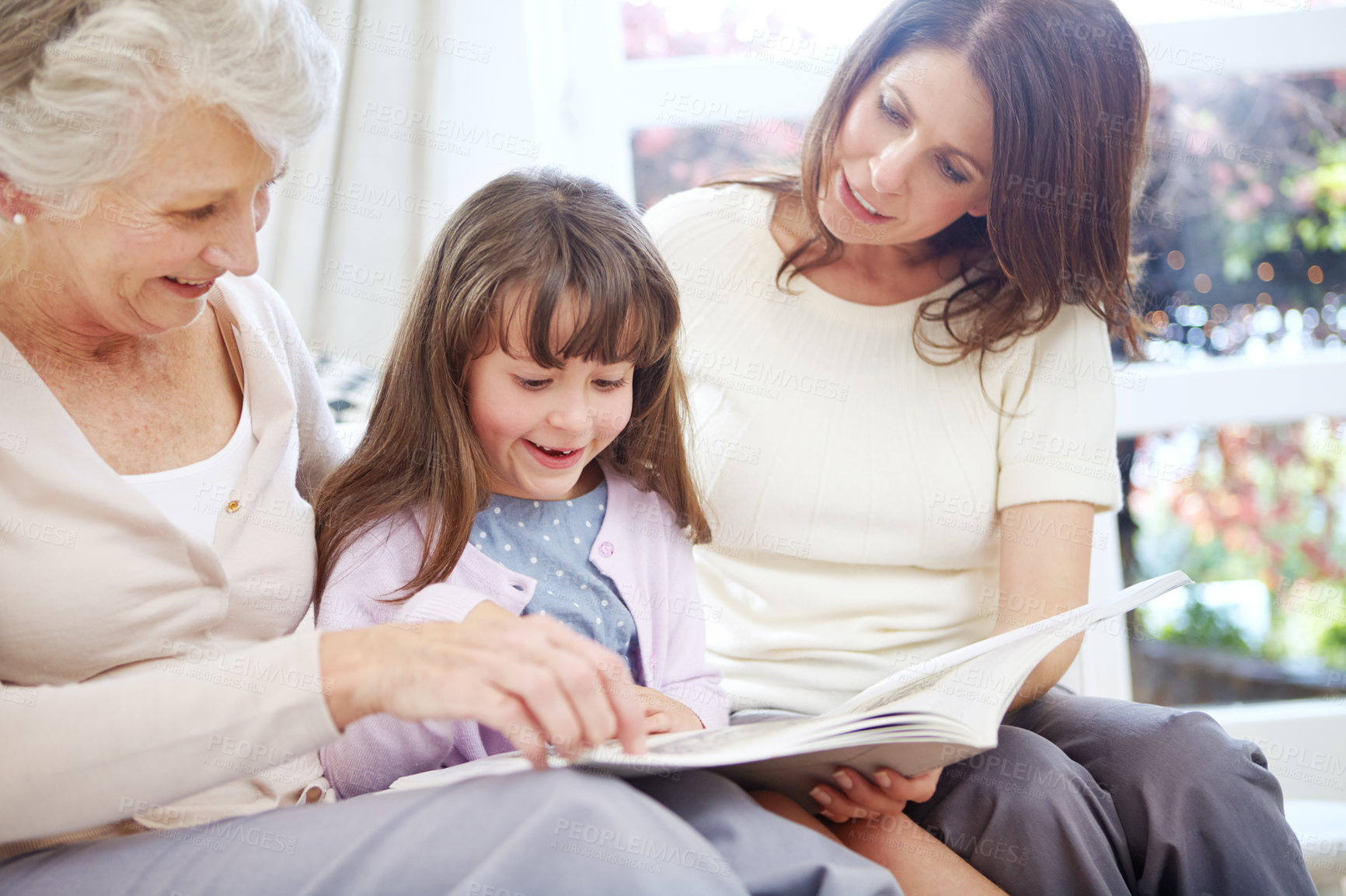 Buy stock photo Reading, story and child with mom and grandmother on sofa in living room for bonding together. Happy, relax and girl with mother and senior woman enjoying fantasy book, novel or literature at home.