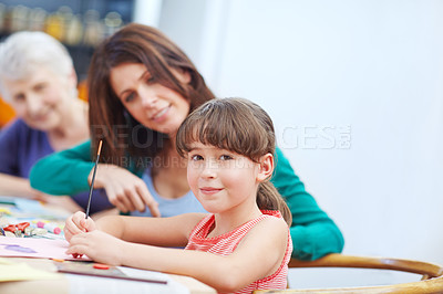 Buy stock photo Shot of a little girl being artistic with her mother and grandmother in the background