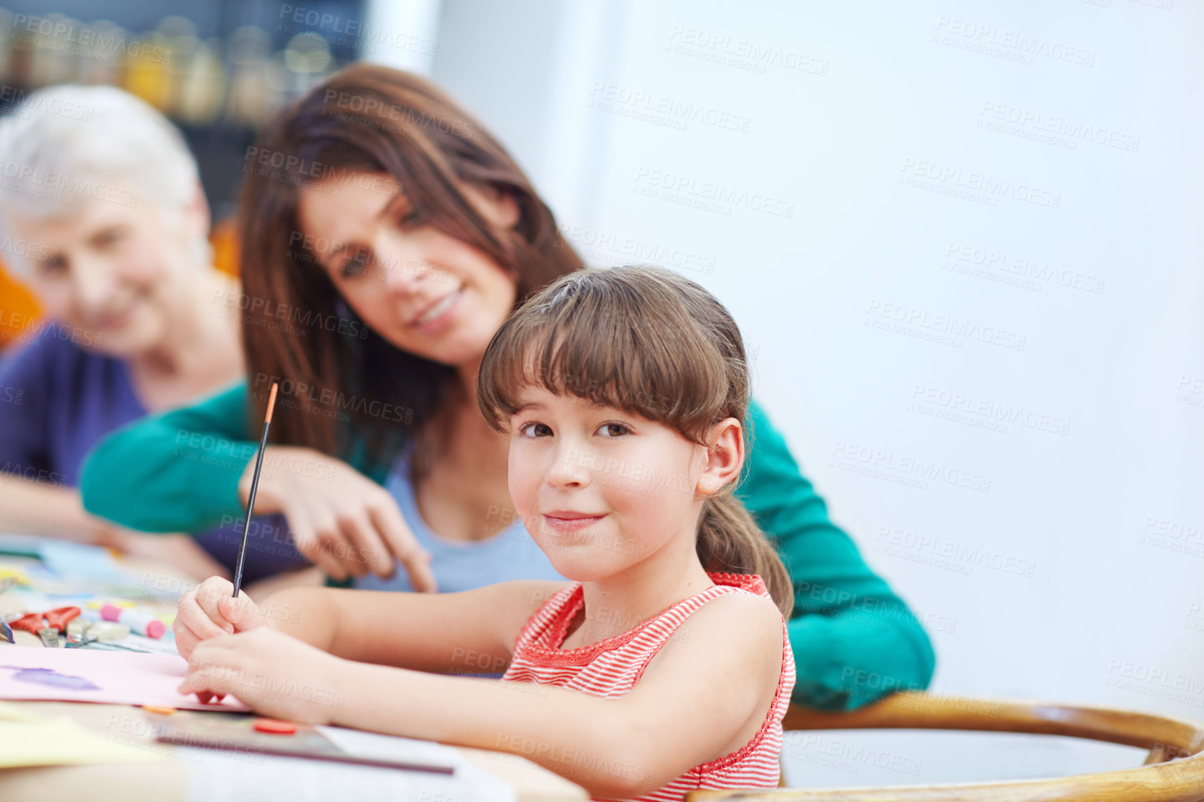 Buy stock photo Shot of a little girl being artistic with her mother and grandmother in the background