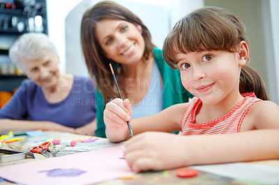 Buy stock photo Shot of a little girl being artistic with her mother and grandmother in the background