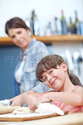 Buy stock photo A cute little girl working with cookie dough with her mother standing in the background