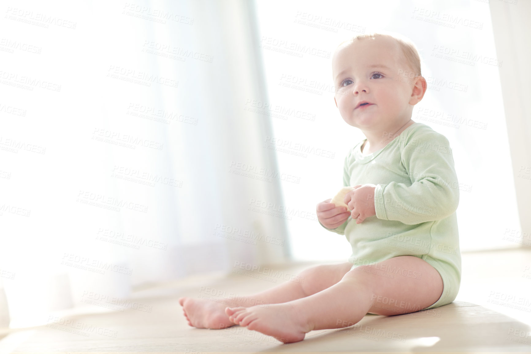 Buy stock photo Shot of a baby boy sitting on the floor while eating a snack