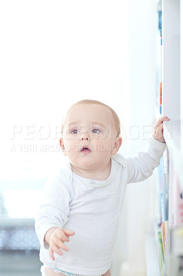 Buy stock photo Shot of an adorable baby boy standing by a bookshelf