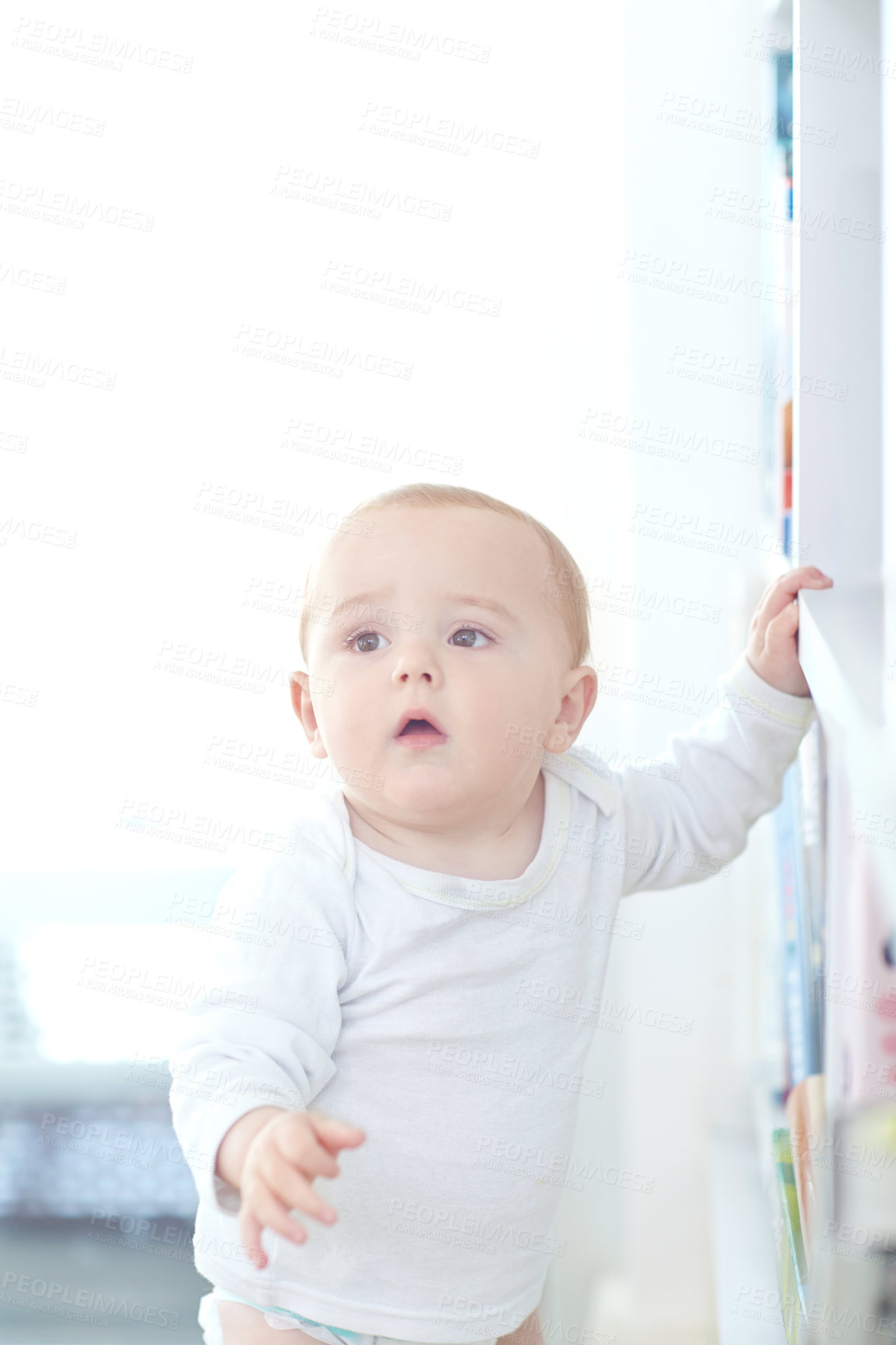 Buy stock photo Shot of an adorable baby boy standing by a bookshelf